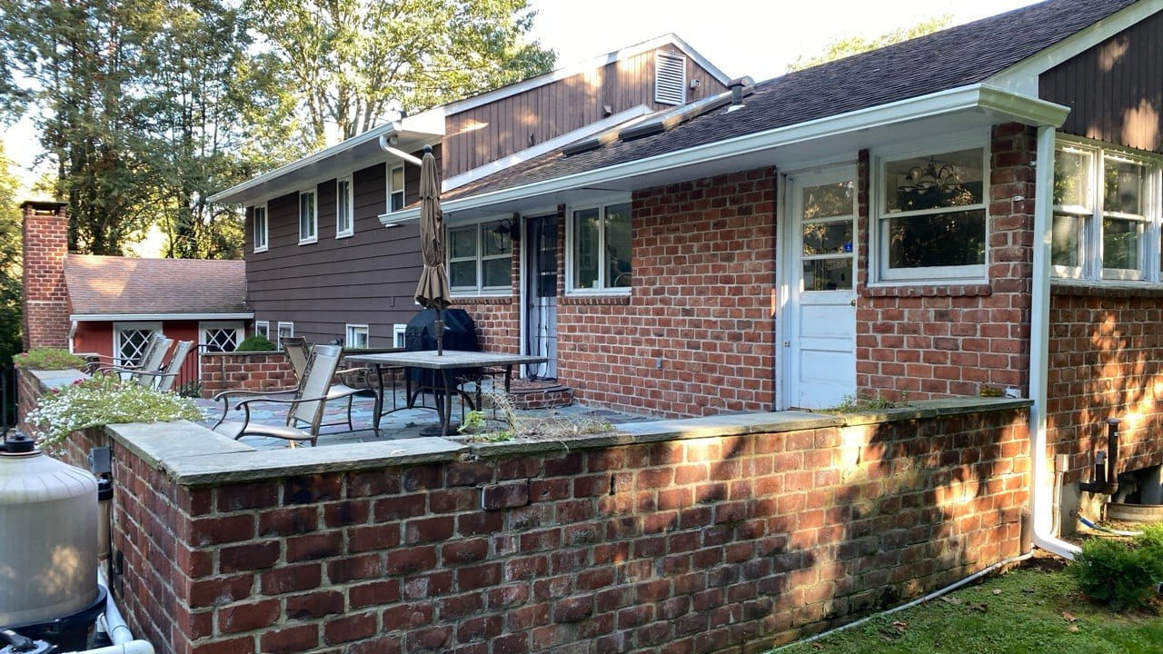 Brick patio home with white gutters on lower roofline and stone retaining wall — Westchester County gutter repair
