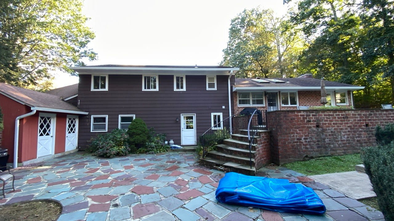 Gutter repair on dark brown siding home with brick addition and detached red garage — Westchester County