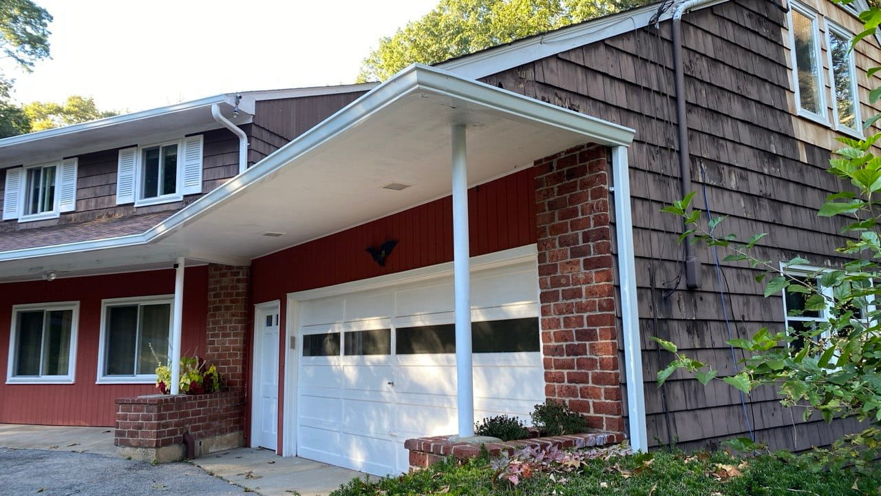 Gutter repair on garage canopy with red wood siding and brick columns — Connecticut residential project