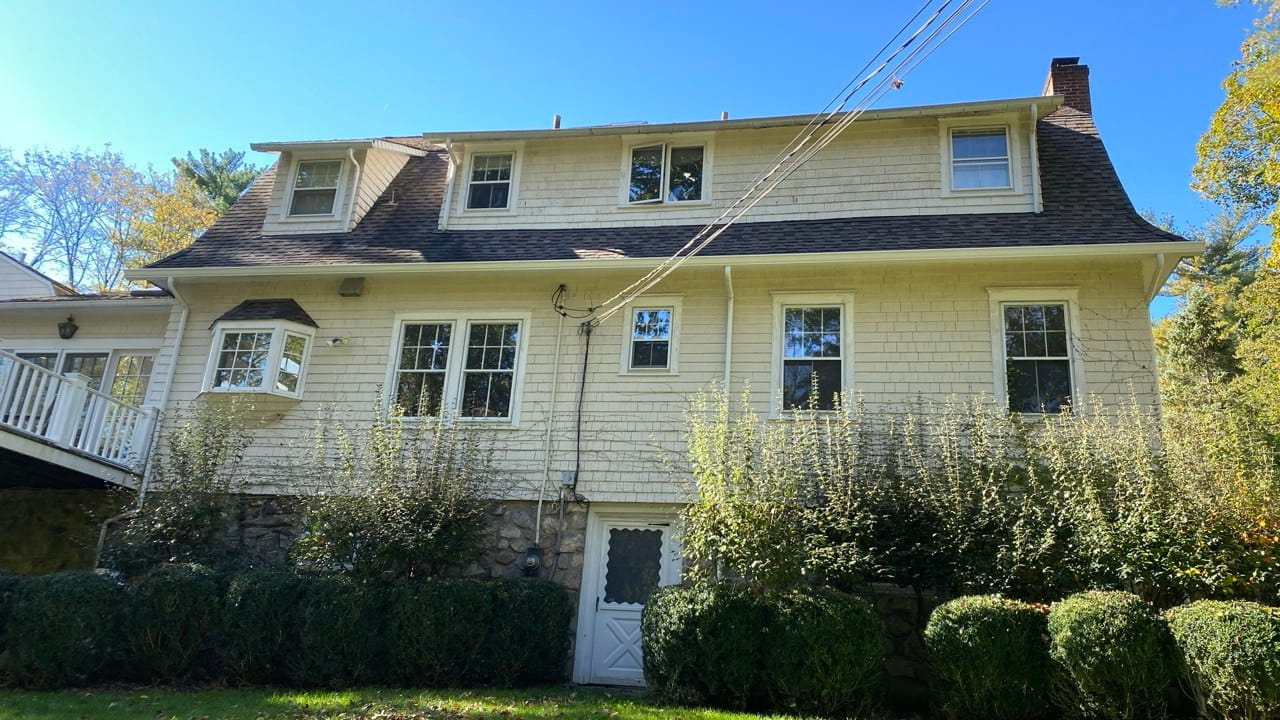 Three-story cedar shingle New England home with white gutters along mansard roofline — Connecticut gutter repair project