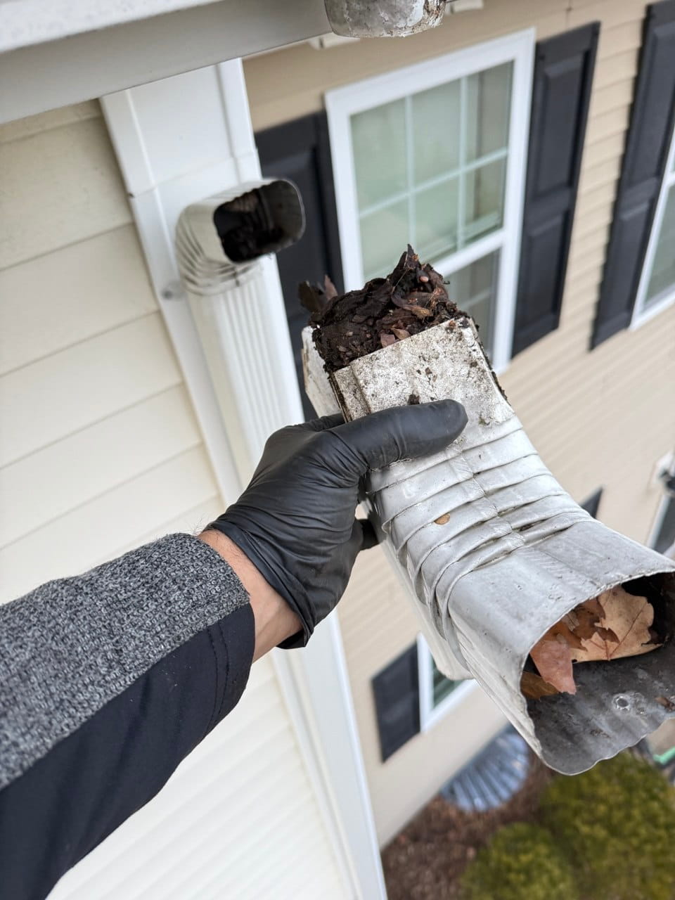 Technician holding a crushed and debris-packed downspout section removed during gutter repair inspection